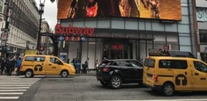 A classic yellow taxi driving past a Seventh Avenue subway entrance in Manhattan, illustrating how to get around NYC.