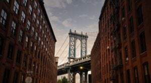 Manhattan Bridge framed by brick buildings in DUMBO, Brooklyn, during sunset.