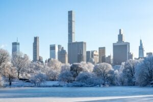 Snow-covered Central Park with a frozen lake and the Midtown Manhattan skyline in winter