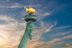 Close view of the Statue of Liberty’s raised arm and torch against a blue sky