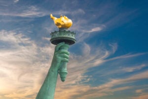 Close view of the Statue of Liberty’s raised arm and torch against a blue sky