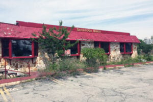 Abandoned Saratoga Diner in Saratoga Springs, New York, showing its red roof, stone exterior, and overgrown entrance in 2016.