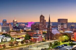 Downtown Syracuse, New York, skyline at dusk with illuminated buildings and a historic church in the foreground.